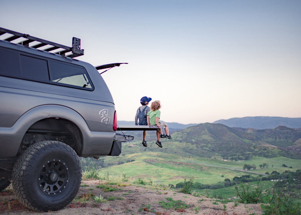 Two children watching a sunset together over a valley on a bedslide in a diesel truck